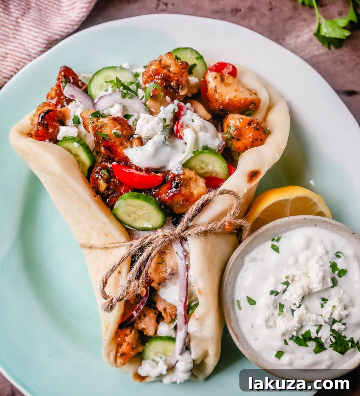 All fresh ingredients for Greek chicken gyros laid out: marinated chicken, grated cucumber for tzatziki, diced vegetables for Greek salad, and pita bread.