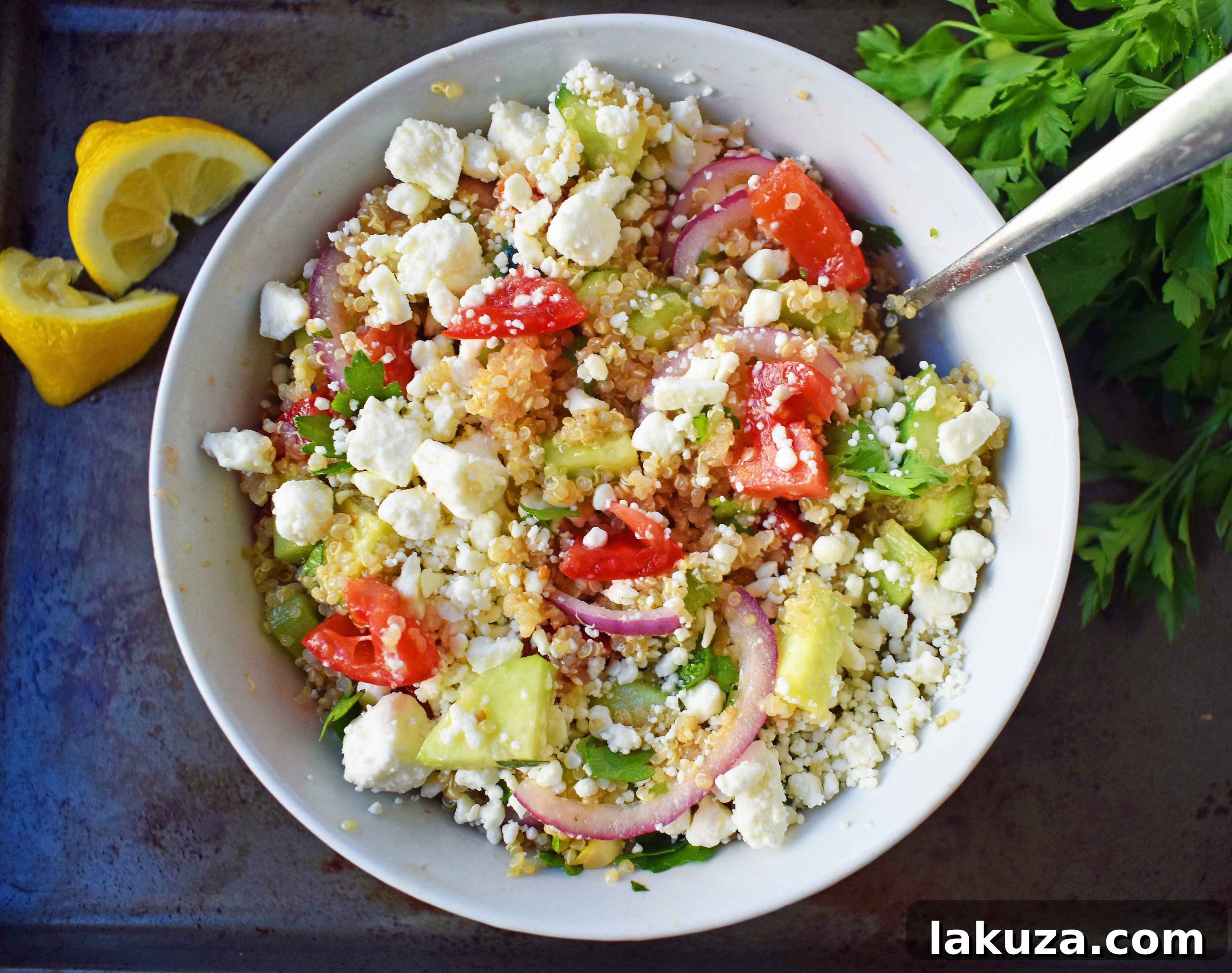 A generous serving of Mediterranean Quinoa Salad, featuring a colorful mix of quinoa, fresh tomatoes, diced cucumber, thinly sliced red onion, and vibrant Italian parsley, dressed with olive oil and red wine vinegar, and topped with rich feta cheese. A healthy, beautiful, and complete meal.