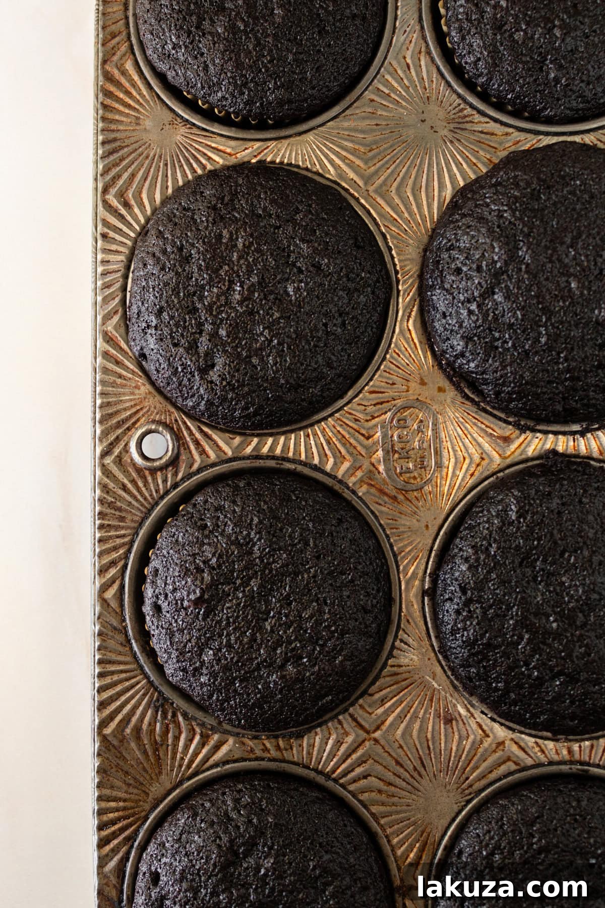 Decadent Chocolate Cupcakes 11 Freshly baked chocolate cupcakes cooling in muffin tins after being removed from the oven.