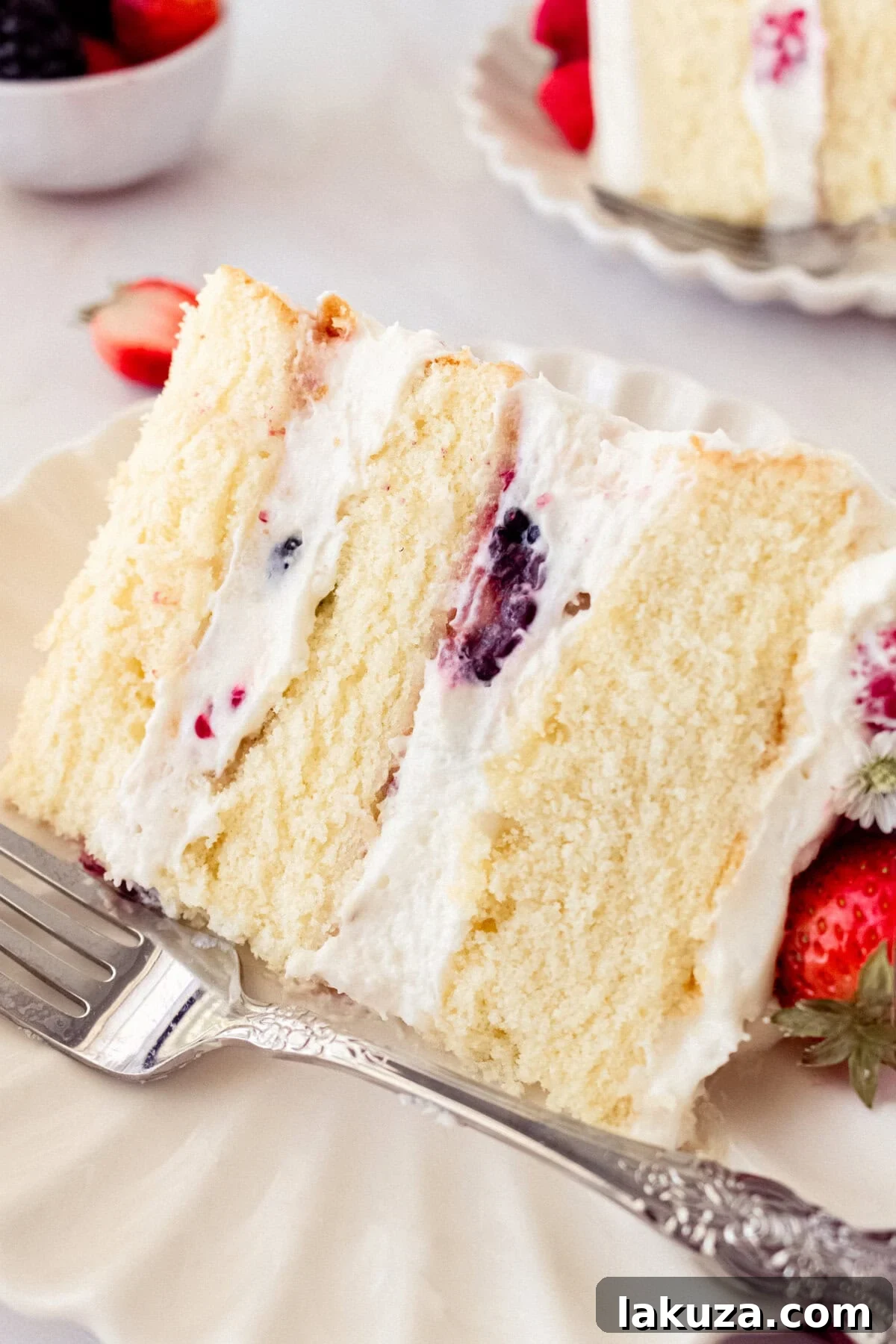 Berry Chantilly Cake 4 A generous slice of Berry Chantilly Cake reveals the perfect balance of golden cake, creamy white frosting, and colorful fruit filling, ready to be enjoyed.