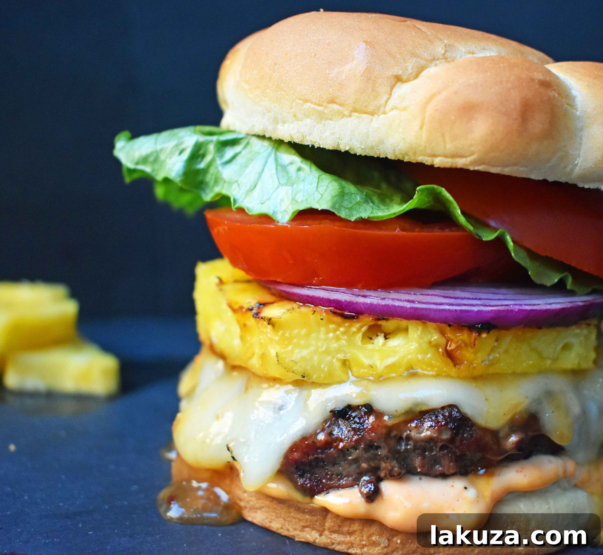 Sweet and Spicy Hawaiian Burger showcasing a perfectly grilled grass-fed beef patty basted with savory Hawaiian pineapple sauce, topped with melted Swiss Cheese and fresh grilled pineapple, all nestled on a toasted bun with Sriracha mayonnaise, crisp lettuce, ripe tomato, and red onion. A taste of Hawaii in every bite!