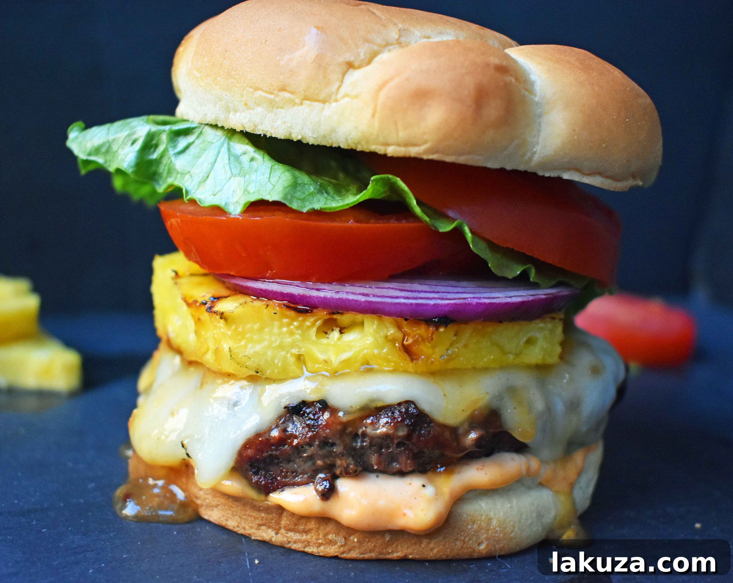 Close-up of a Sweet and Spicy Hawaiian Burger featuring grass-fed beef, grilled to juicy perfection and basted with a vibrant Hawaiian pineapple sauce. Topped with melted Swiss Cheese, a golden grilled pineapple slice, and served on a toasted bun generously coated with Sriracha mayonnaise. Fresh lettuce, tomato, and red onion complete this irresistible tropical burger.