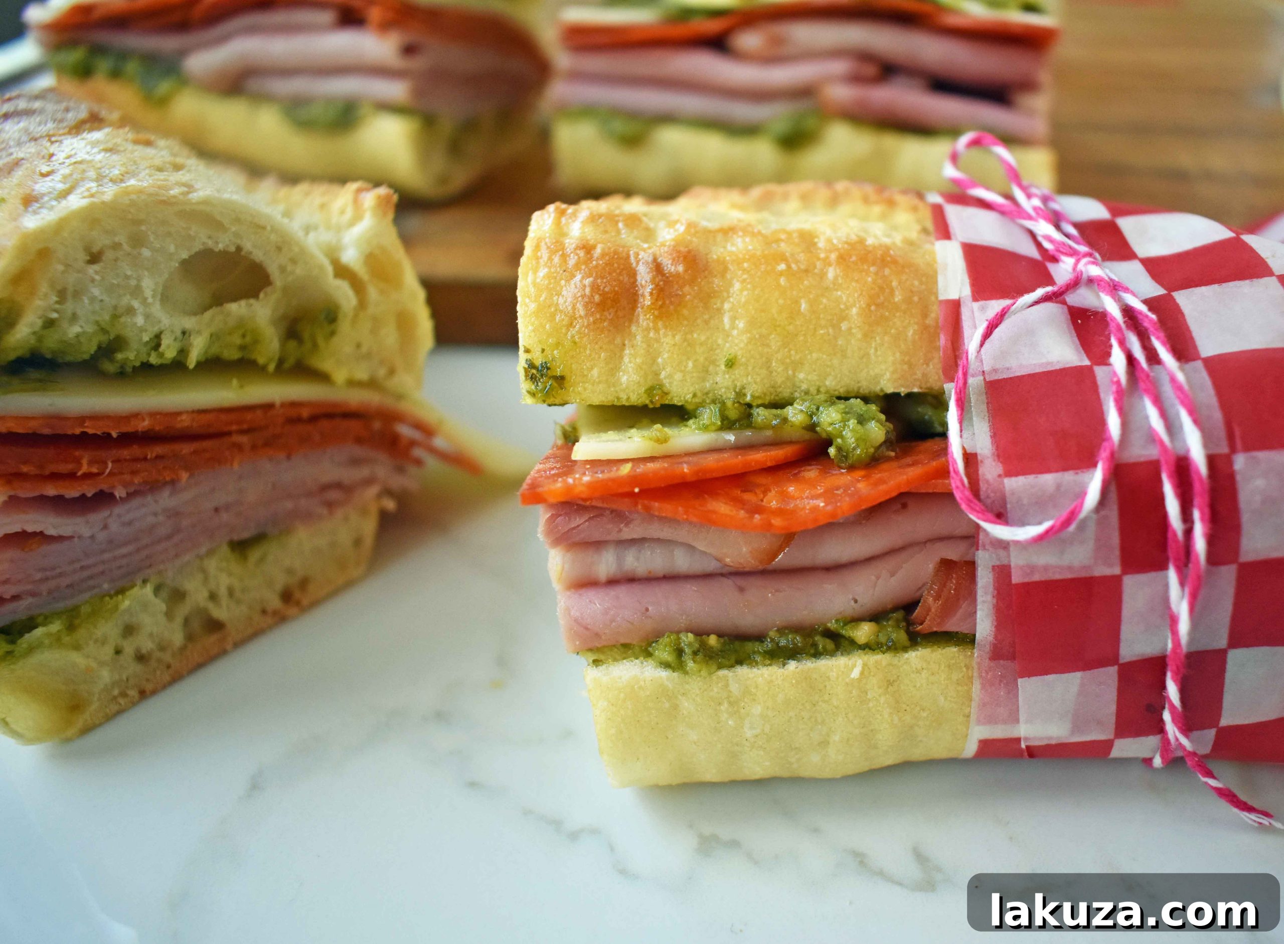 Hand holding a slice of Italian Pressed Sandwich with layers of ham, salami, provolone, and pesto on crusty bread