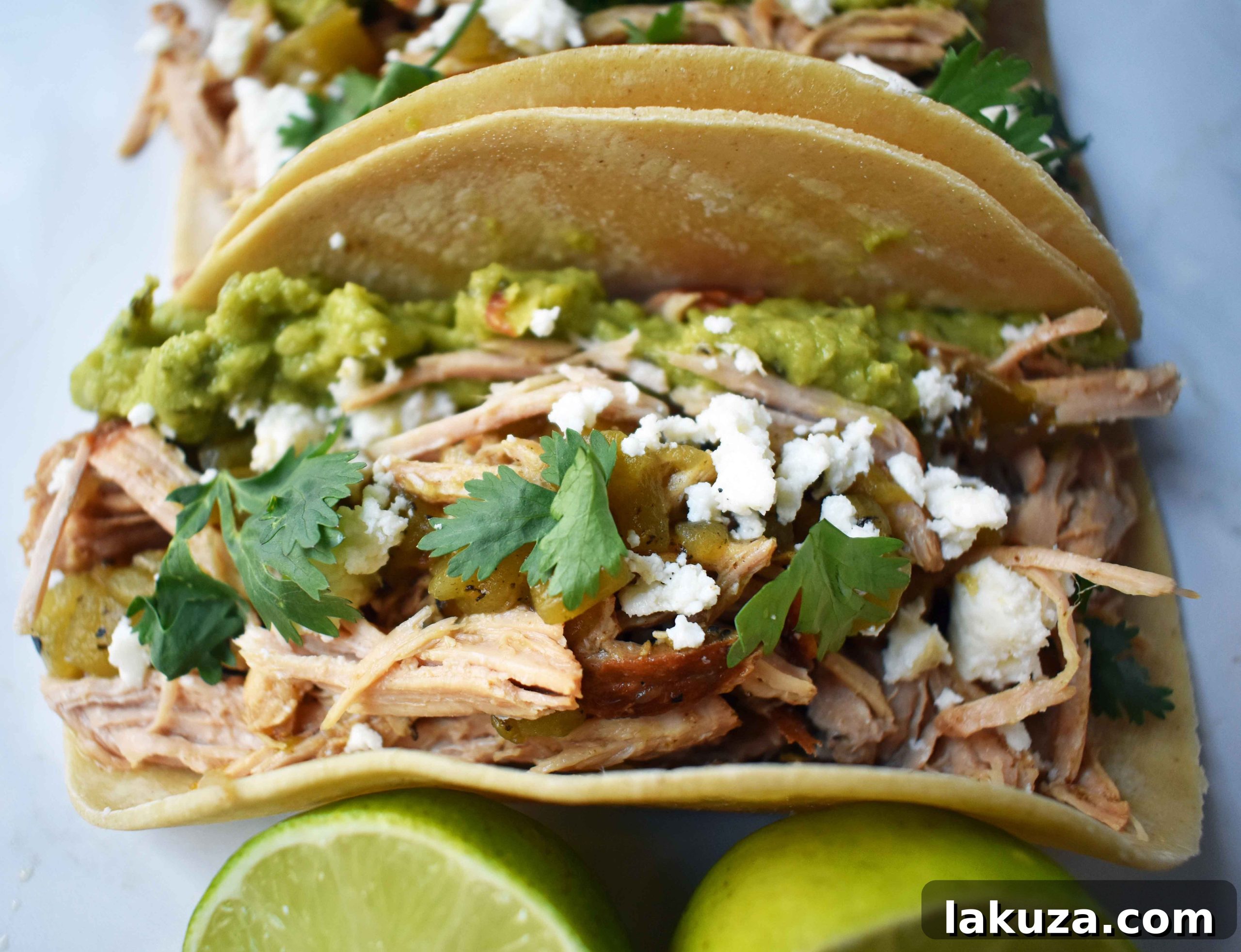 Close-up shot of slow-cooked green chili pork carnitas tacos, showcasing the tender seasoned pork, fresh lime juice glaze, and toppings like cotija cheese, jalapeños, avocado, and cilantro on a warm corn tortilla.
