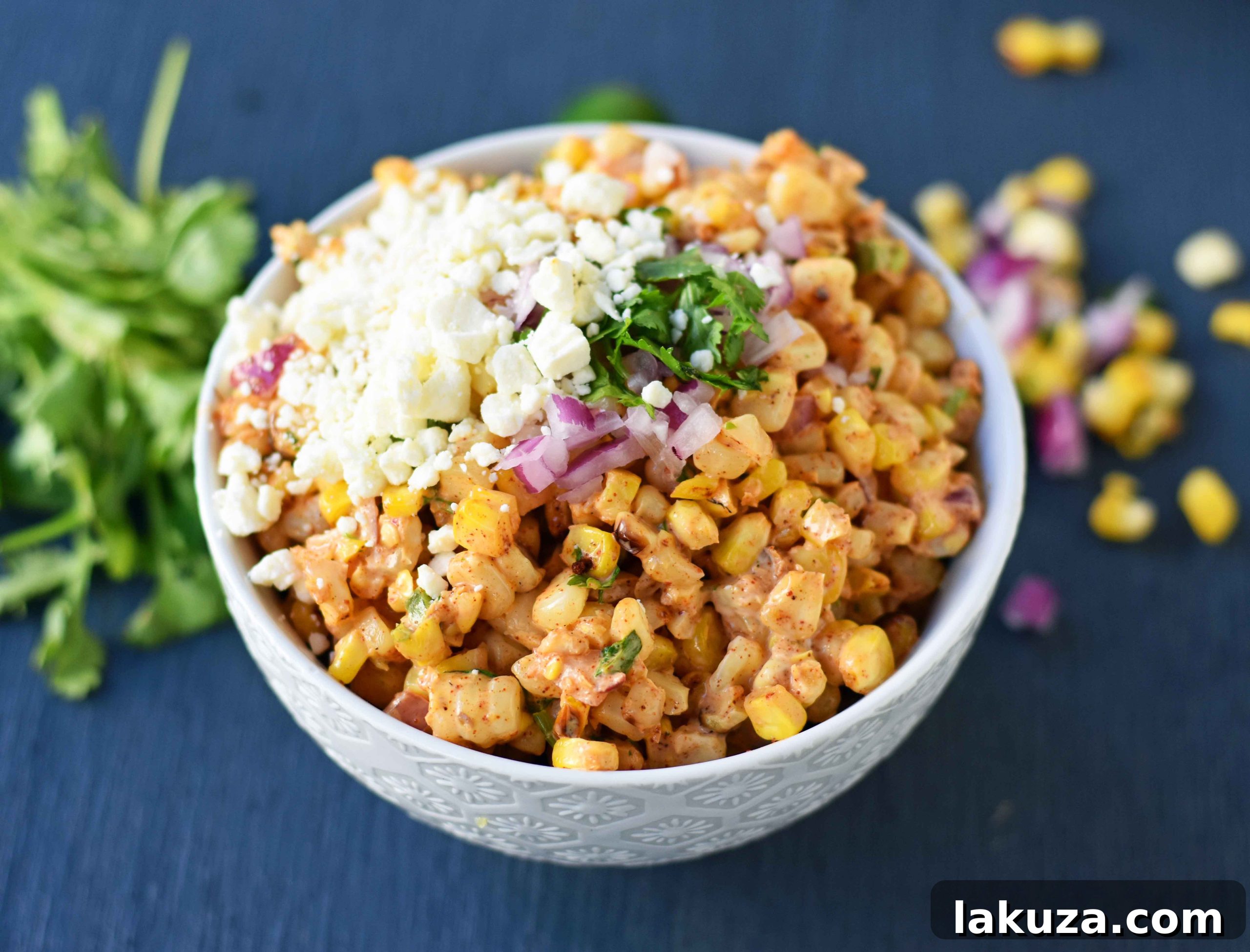 Creamy Elote Dip 6 A large bowl of Mexican Street Corn Salad presented beautifully, with roasted corn, Mexican spices, lime, cilantro, a creamy dressing, and crumbled Cotija cheese, ideal for parties or family meals.