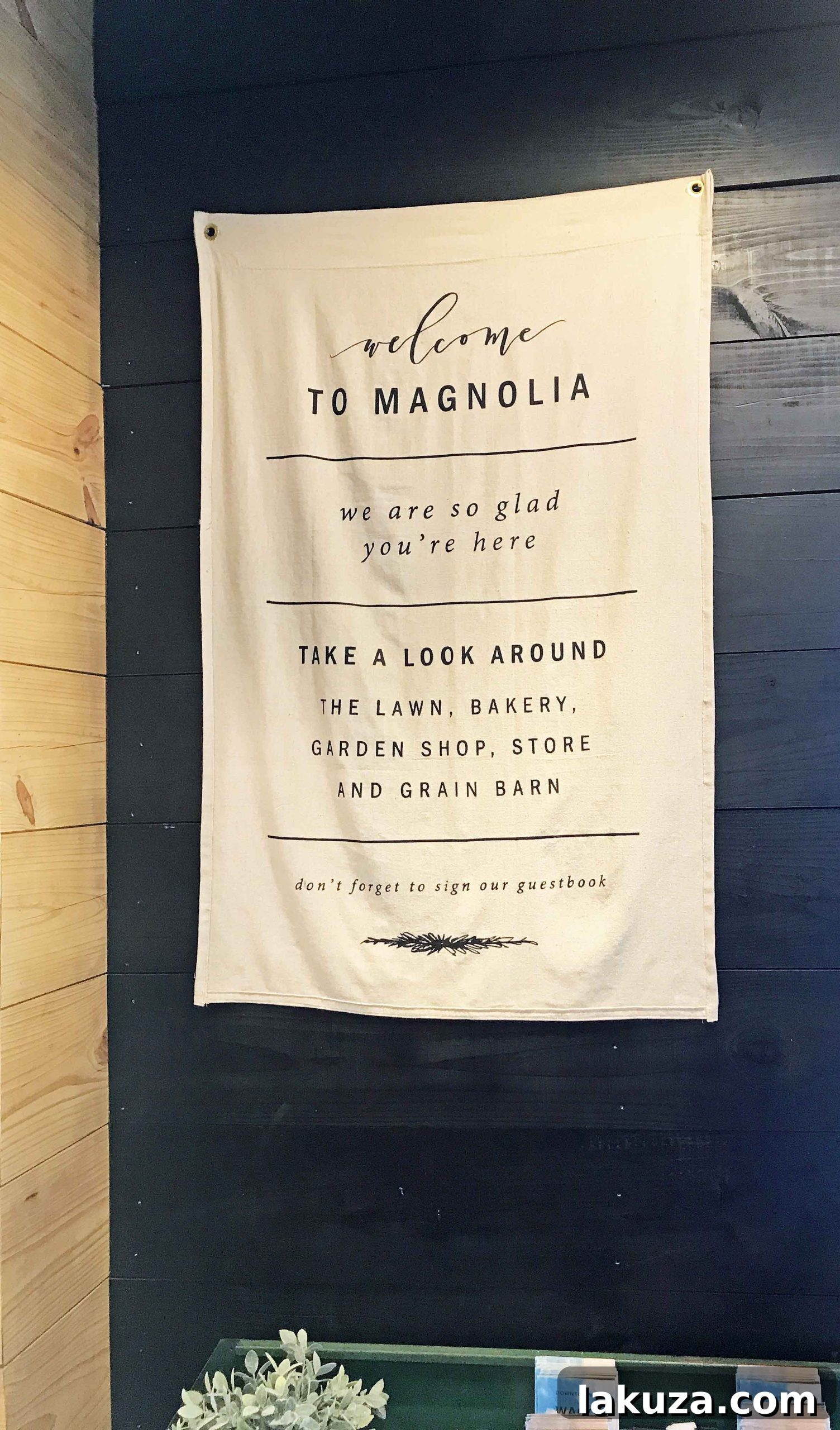 A charming wooden sign detailing the operating hours of Magnolia Market, set amidst greenery