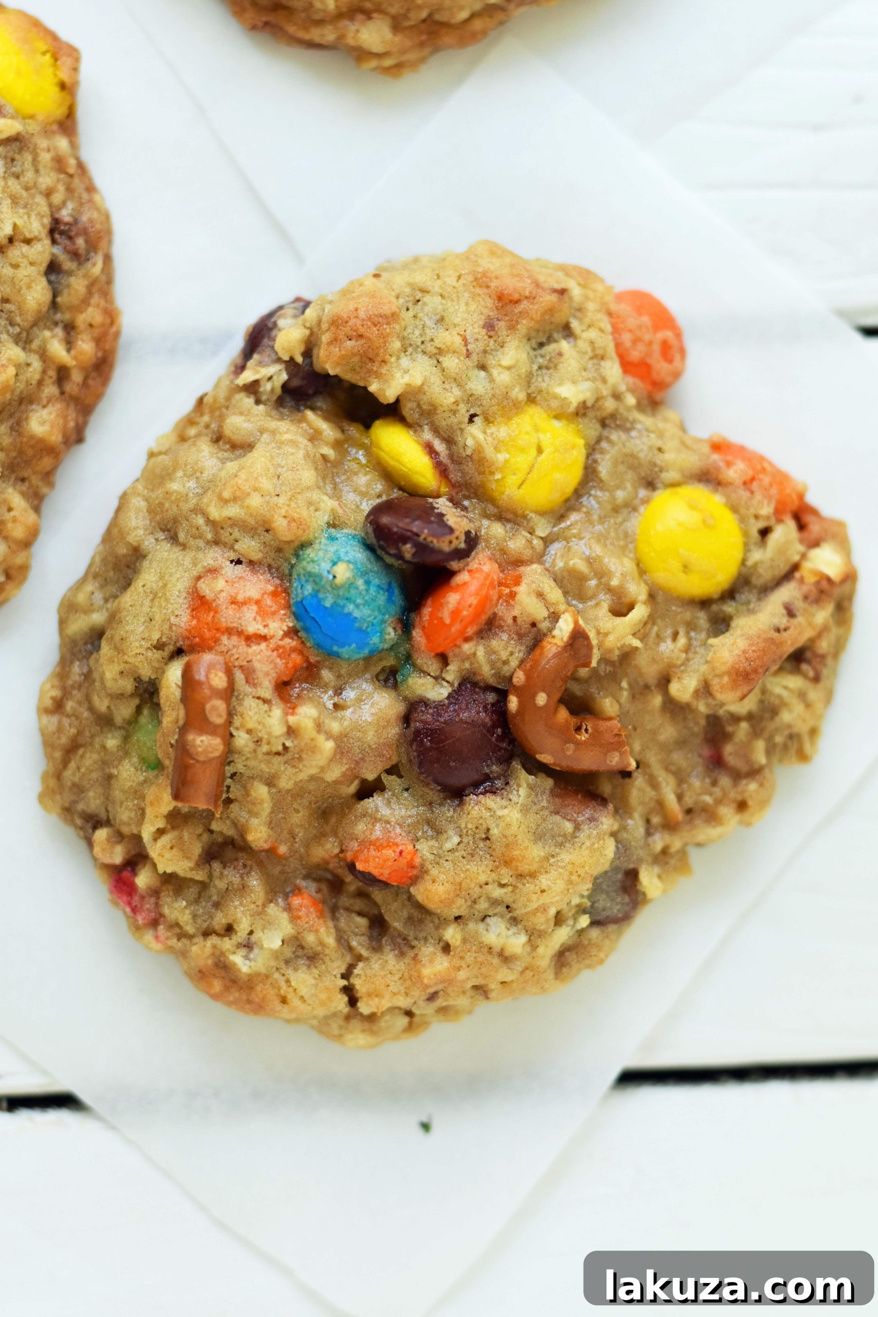 A close-up shot of a single Overachiever Oatmeal Pretzel M&M Cookie, showing the intricate mix of ingredients and its perfectly baked, slightly golden appearance.