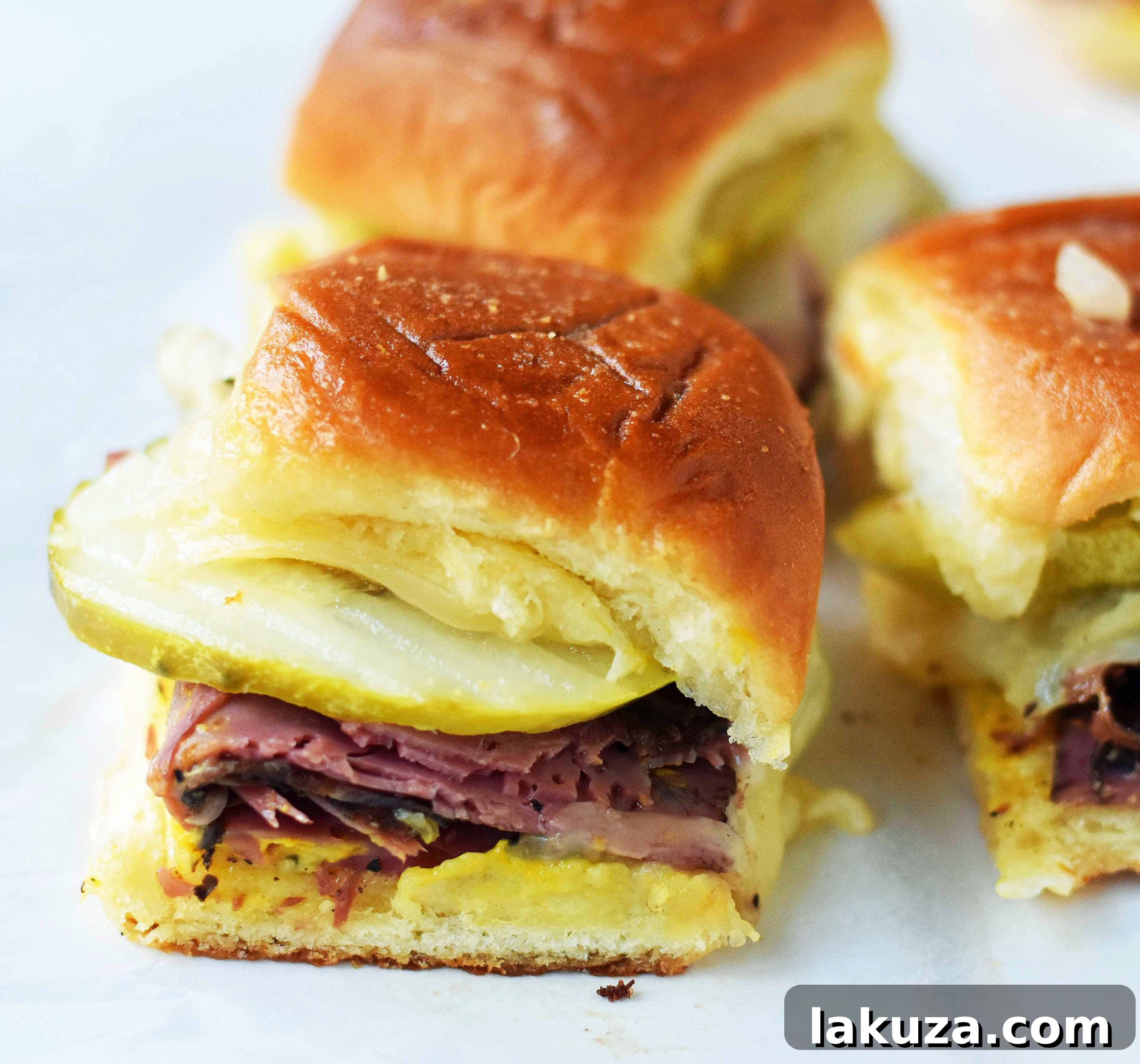 Tailgate Touchdown Hot Pastrami and Swiss Sliders 3 Close-up of baked Hot Pastrami and Swiss Tailgate Sliders. Golden brown Hawaiian rolls basted with garlic butter, filled with layers of pastrami and melted Swiss cheese, ready to be served. Ideal for entertaining or a casual meal.