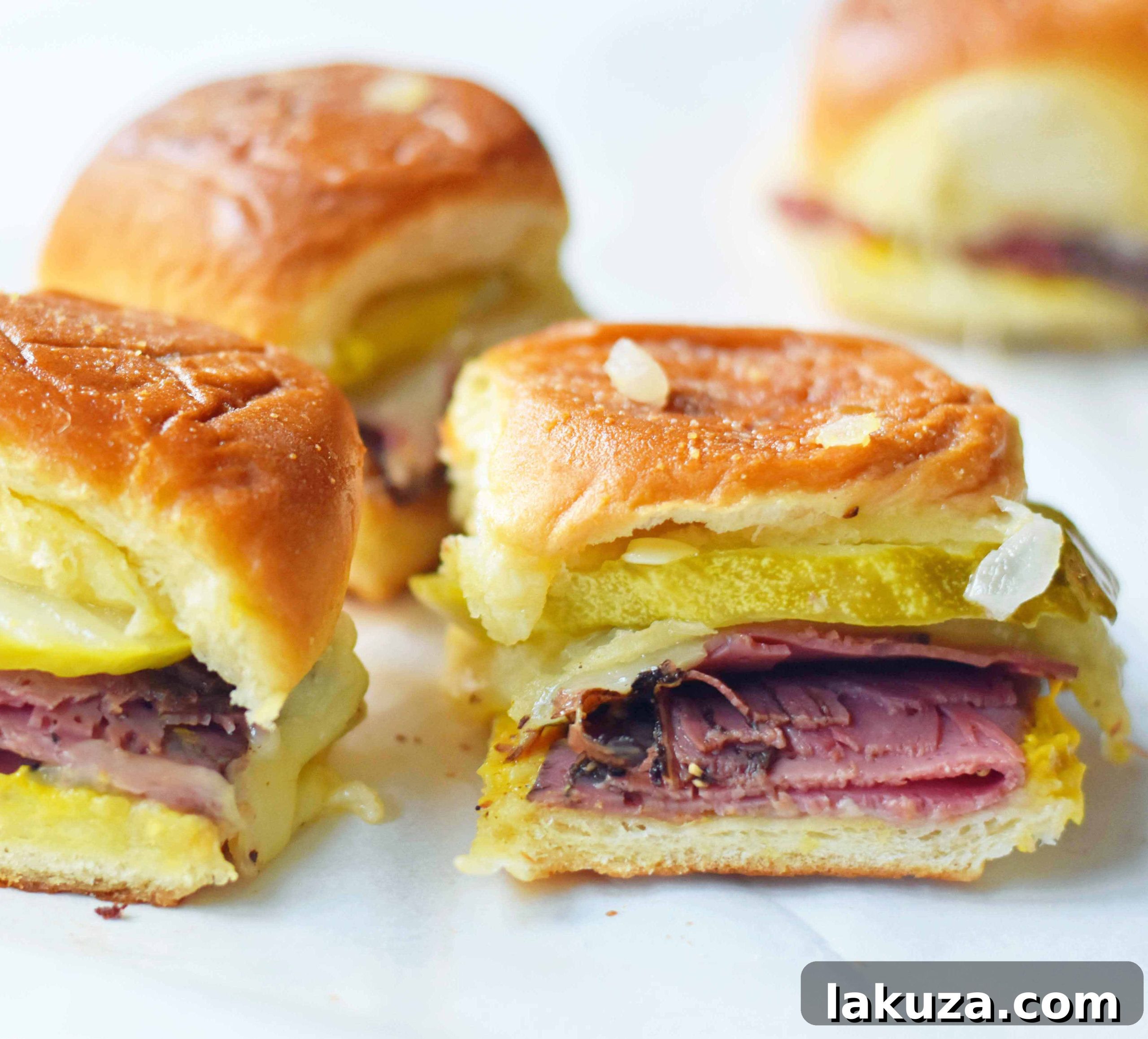 Tailgate Touchdown Hot Pastrami and Swiss Sliders 4 Assortment of Hot Pastrami and Swiss Tailgate Sliders, garnished with dill pickle slices, ready for serving. The golden tops of the rolls and visible melted cheese hint at their delicious warmth.