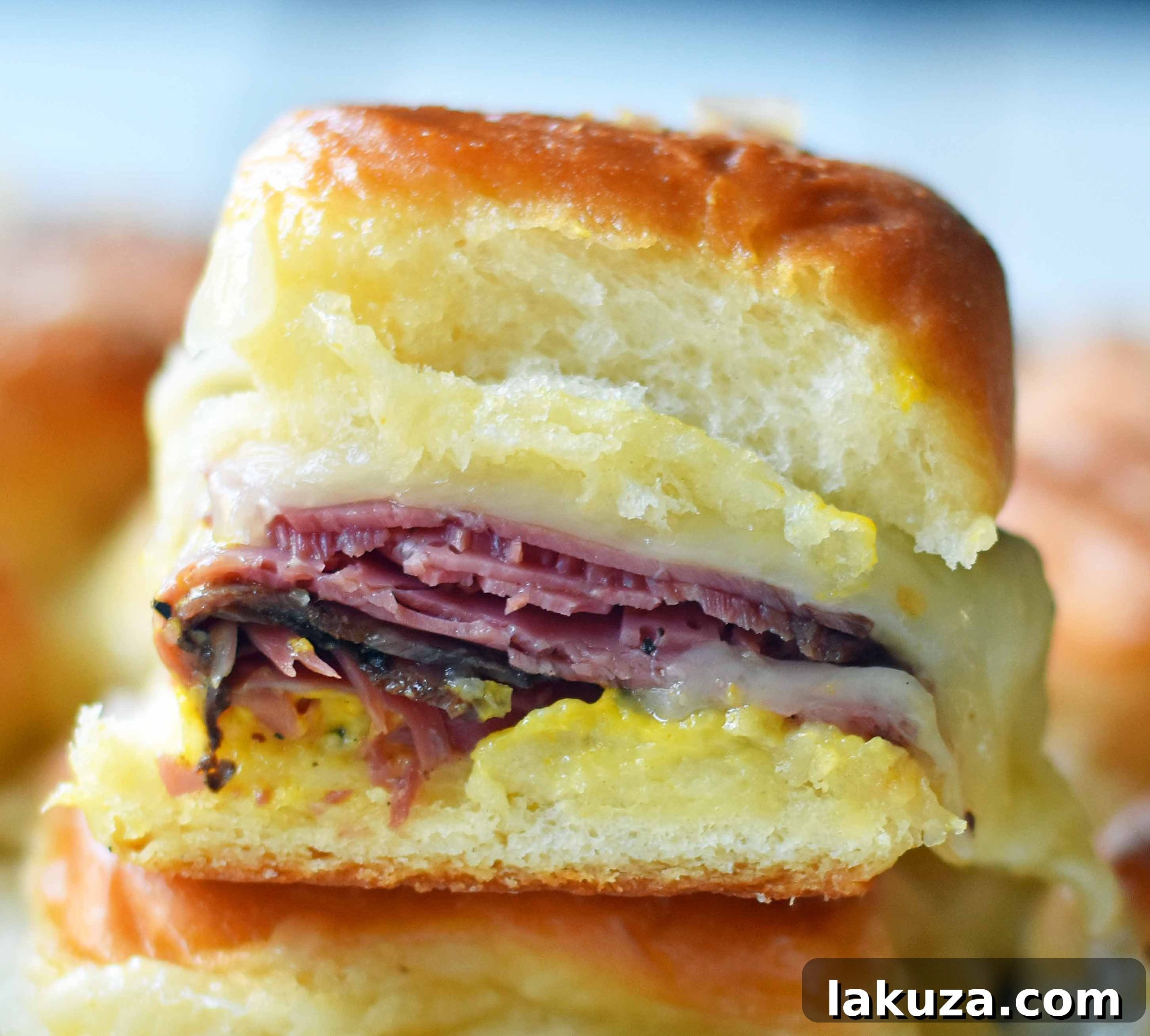 Tailgate Touchdown Hot Pastrami and Swiss Sliders 5 Finished plate of Hot Pastrami and Swiss Tailgate Sliders, cut and ready to eat, with a side of dill pickles. The soft, buttery rolls are perfectly toasted, showing melted cheese and pastrami inside.