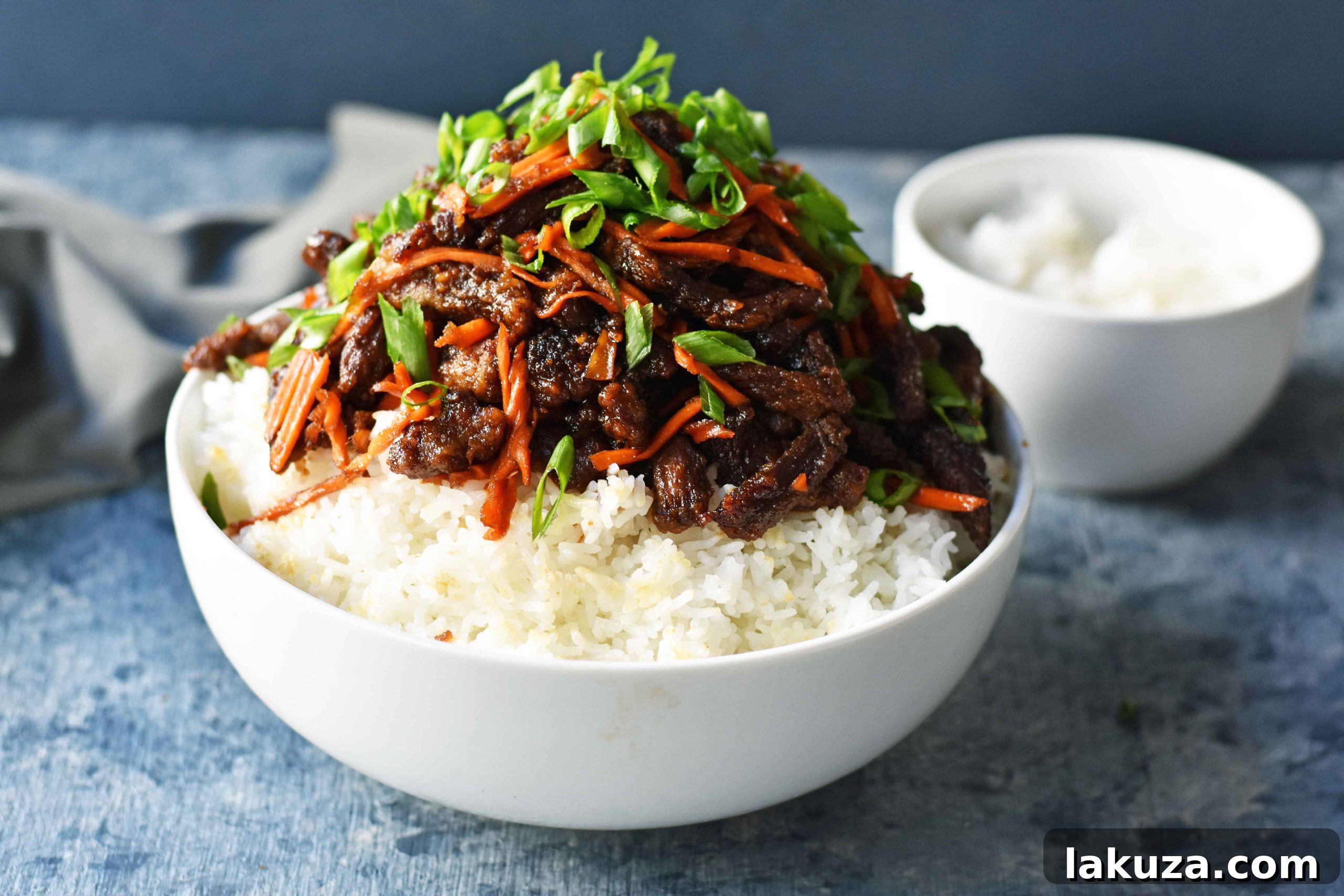 Close-up of crispy Mongolian Beef in a sticky brown sauce, garnished with fresh green onions.