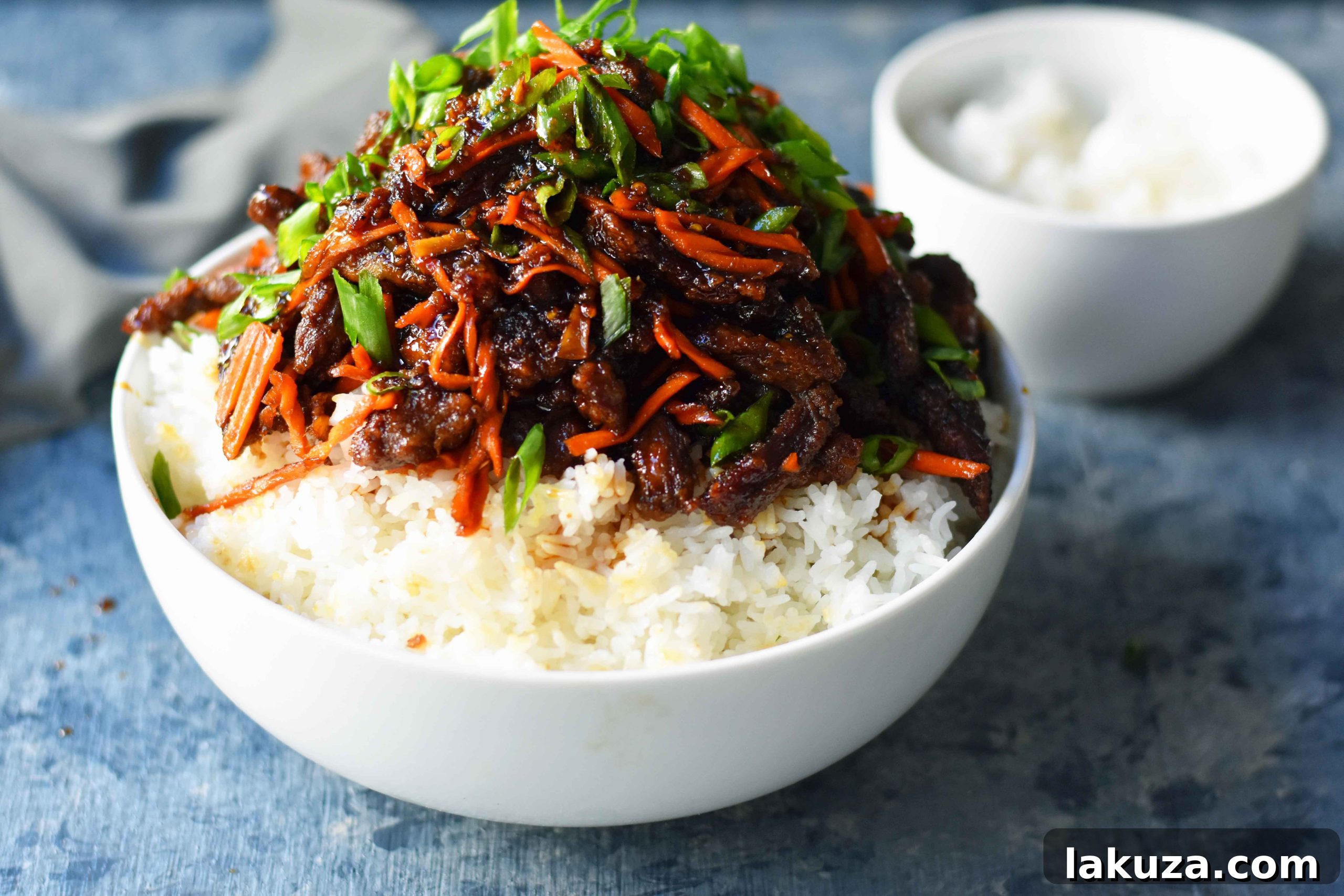 A serving of P.F. Chang's style Mongolian Beef, with rice, garnished with green onions and carrots.