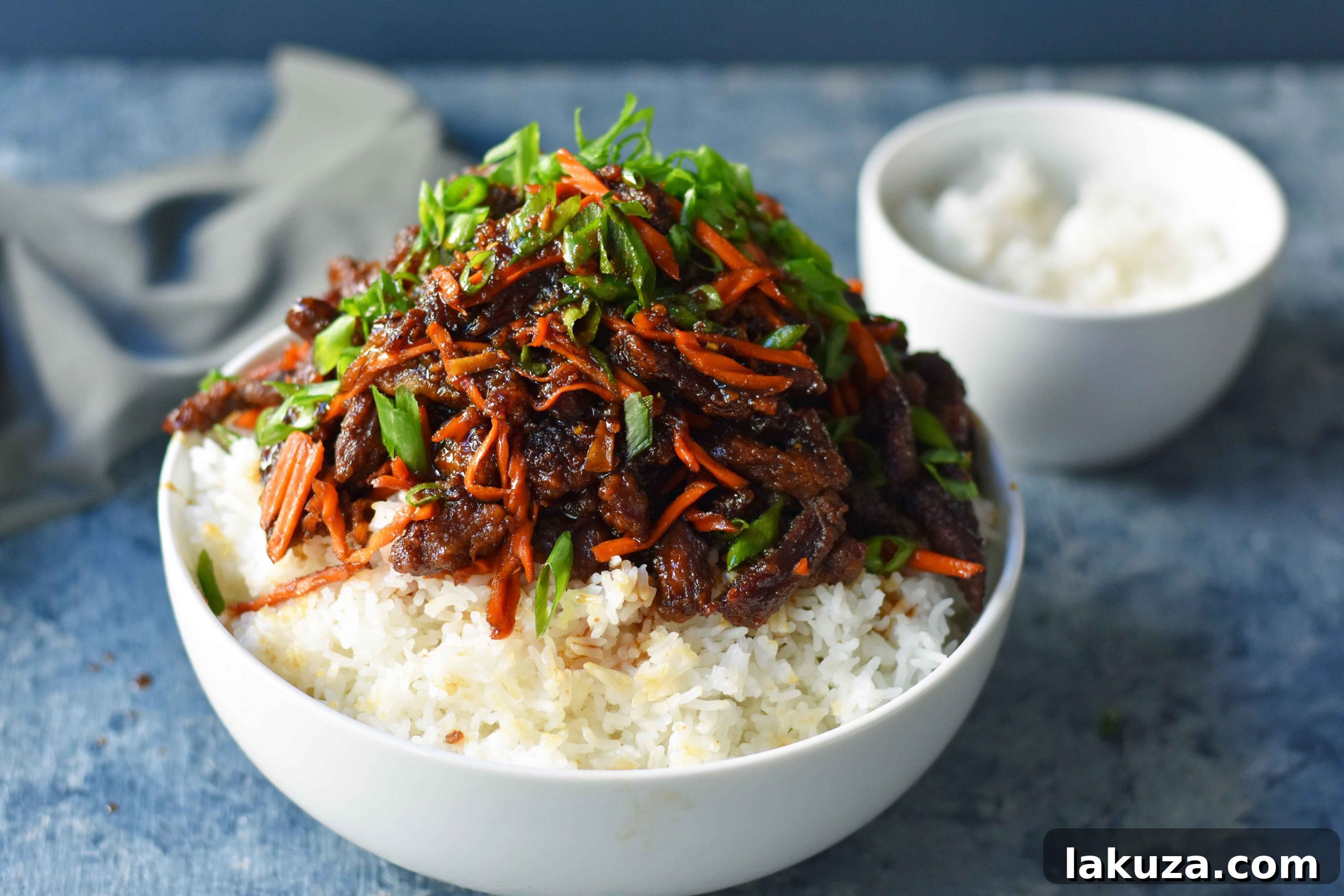 Freshly cooked Mongolian Beef plated with white rice, green onions, and shredded carrots ready to be served.