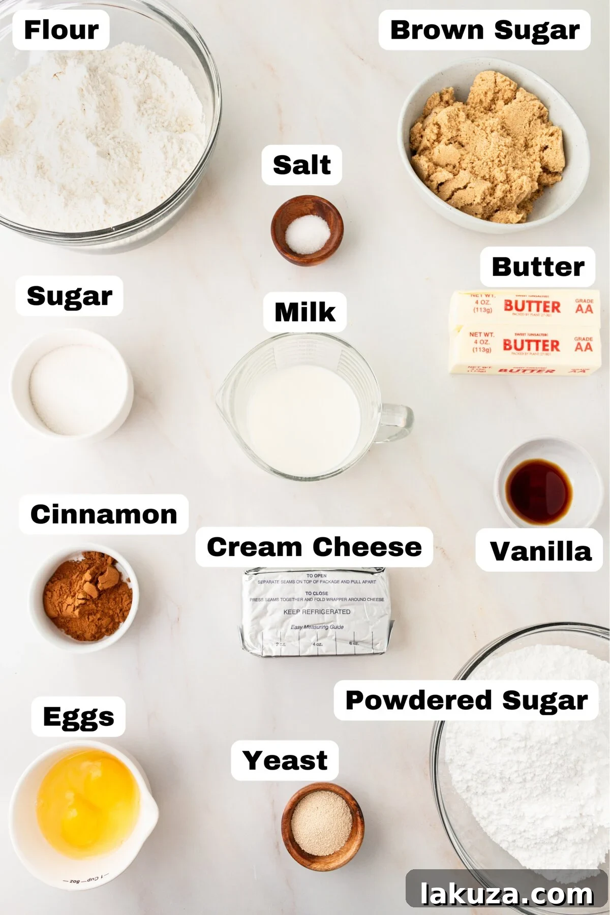 Heavenly Homemade Cinnamon Buns 5 A collection of key ingredients for homemade cinnamon rolls laid out, including milk, yeast, sugar, eggs, butter, salt, flour, brown sugar, cinnamon, cream cheese, and powdered sugar.