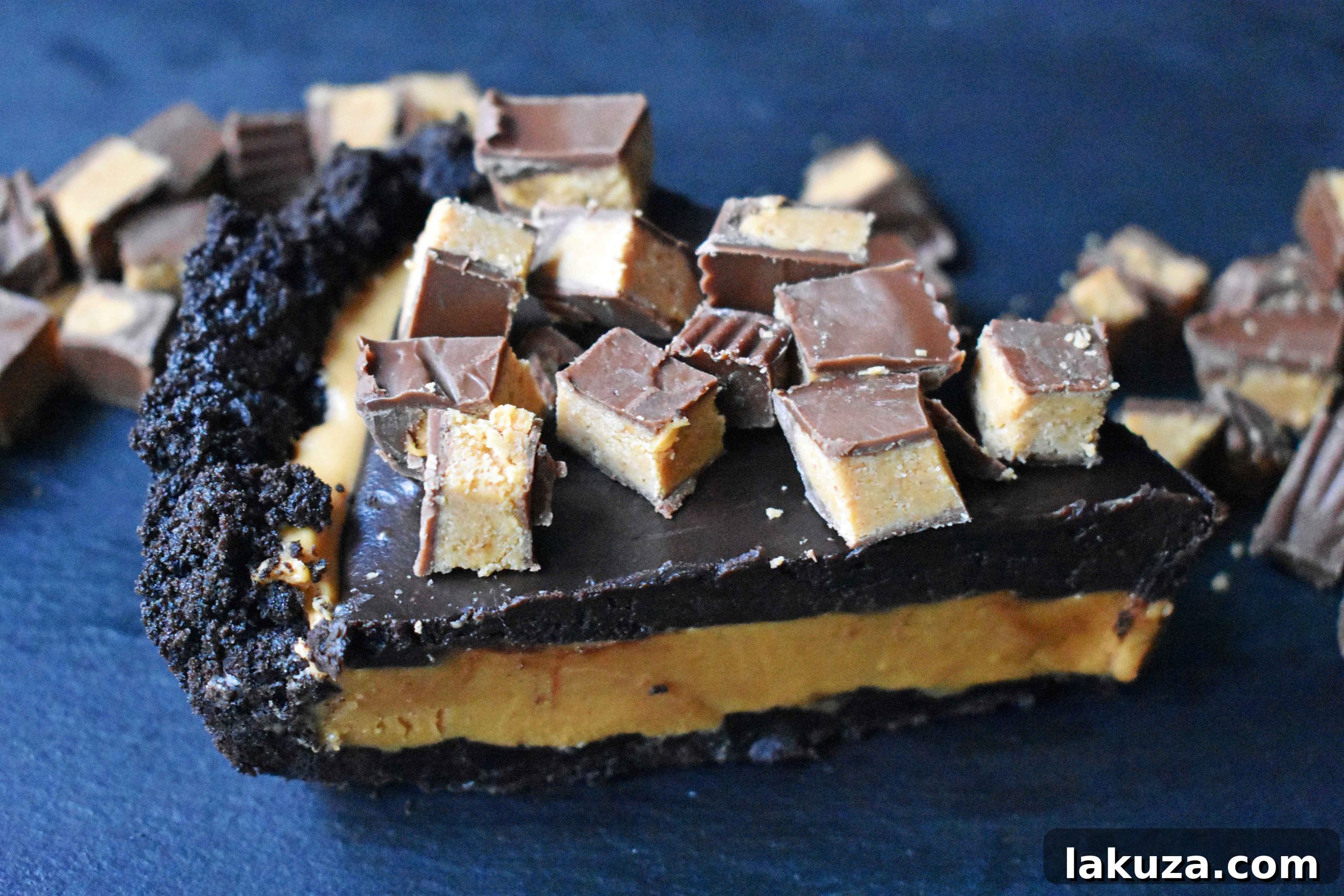 Close-up of a homemade no-bake Reese's Chocolate Peanut Butter Cup Pie, showcasing the vibrant layers of OREO crust, peanut butter filling, and chocolate ganache with chopped Reese's on top.