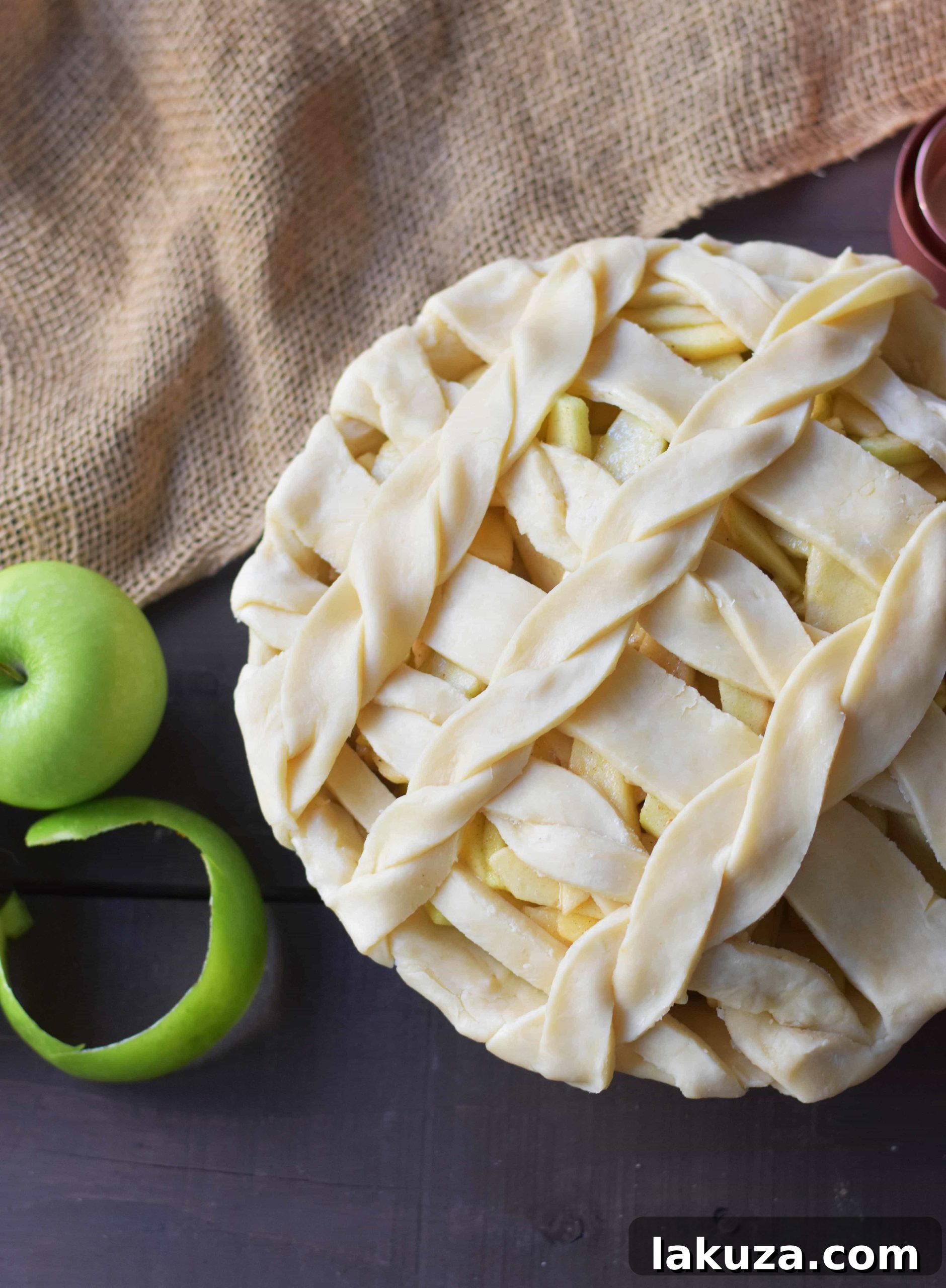 A whole salted caramel apple pie with a perfectly woven lattice crust, sitting on a rustic wooden surface, highlighting its artisanal quality.