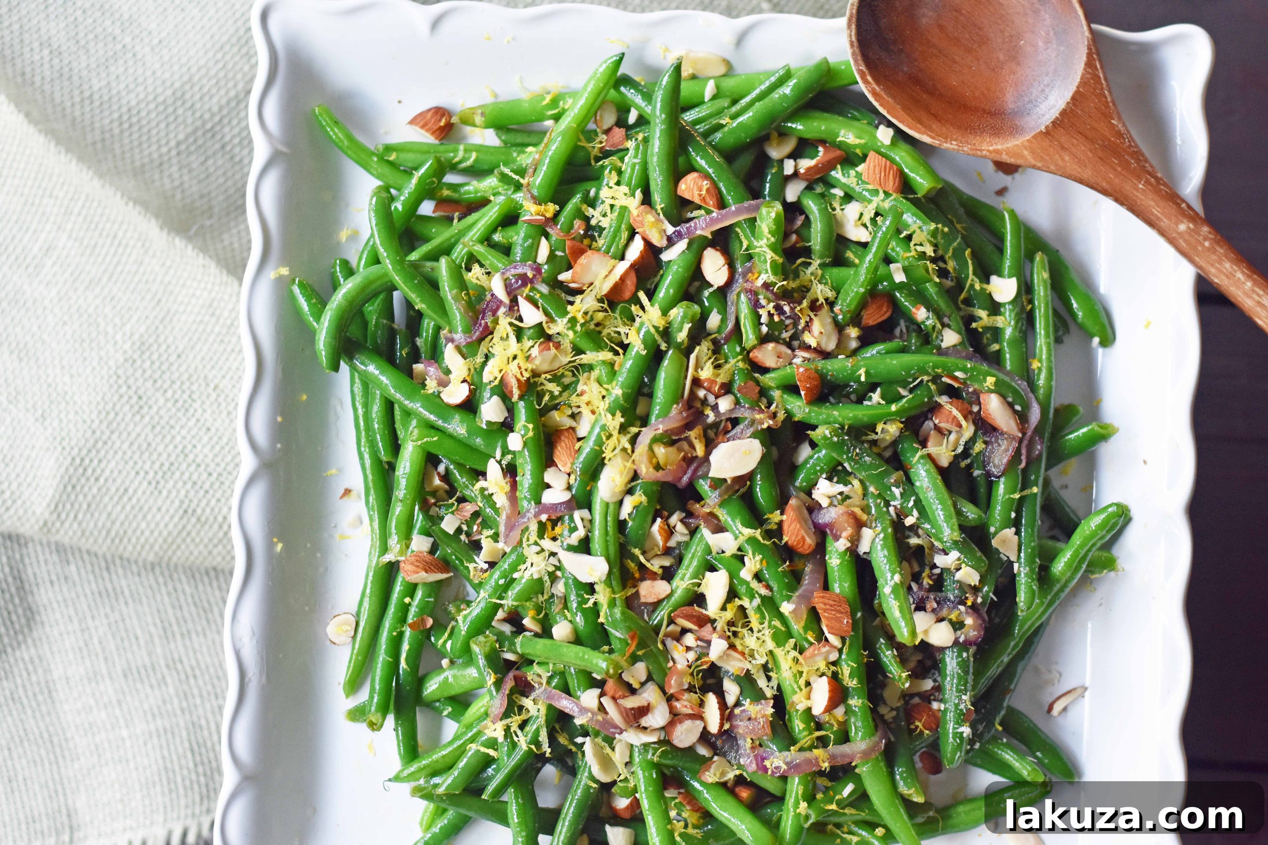 Vibrant green beans sautéed with golden caramelized onions, bright lemon zest, and crunchy almonds, creating a sophisticated and healthy side dish for holiday gatherings or weeknight dinners. Modern Honey recipe.