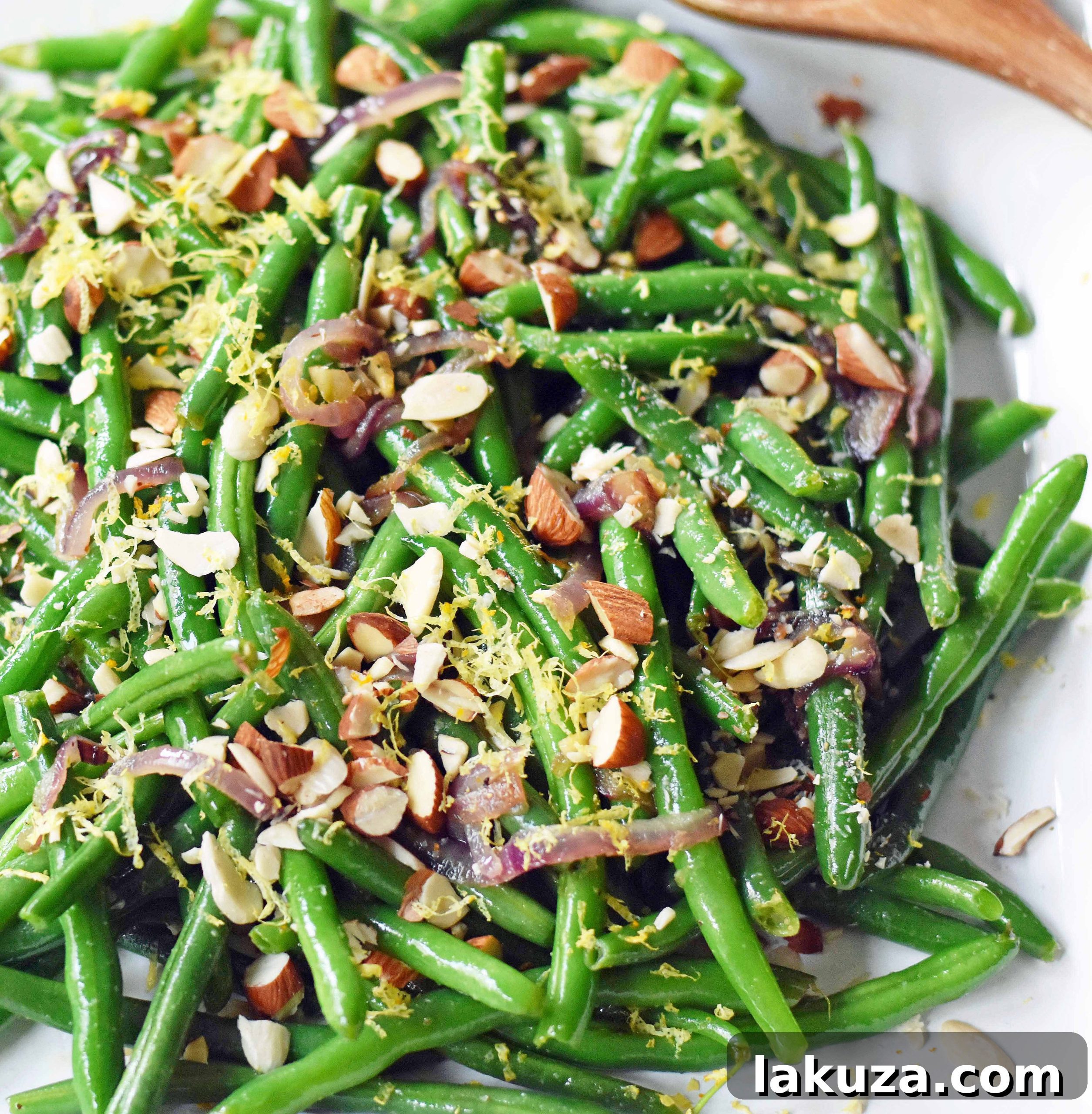 A serving of Green Beans Almondine, perfectly garnished with lemon zest and chopped almonds, ready to be enjoyed as a light and fresh side dish for any occasion. Modern Honey recipe.