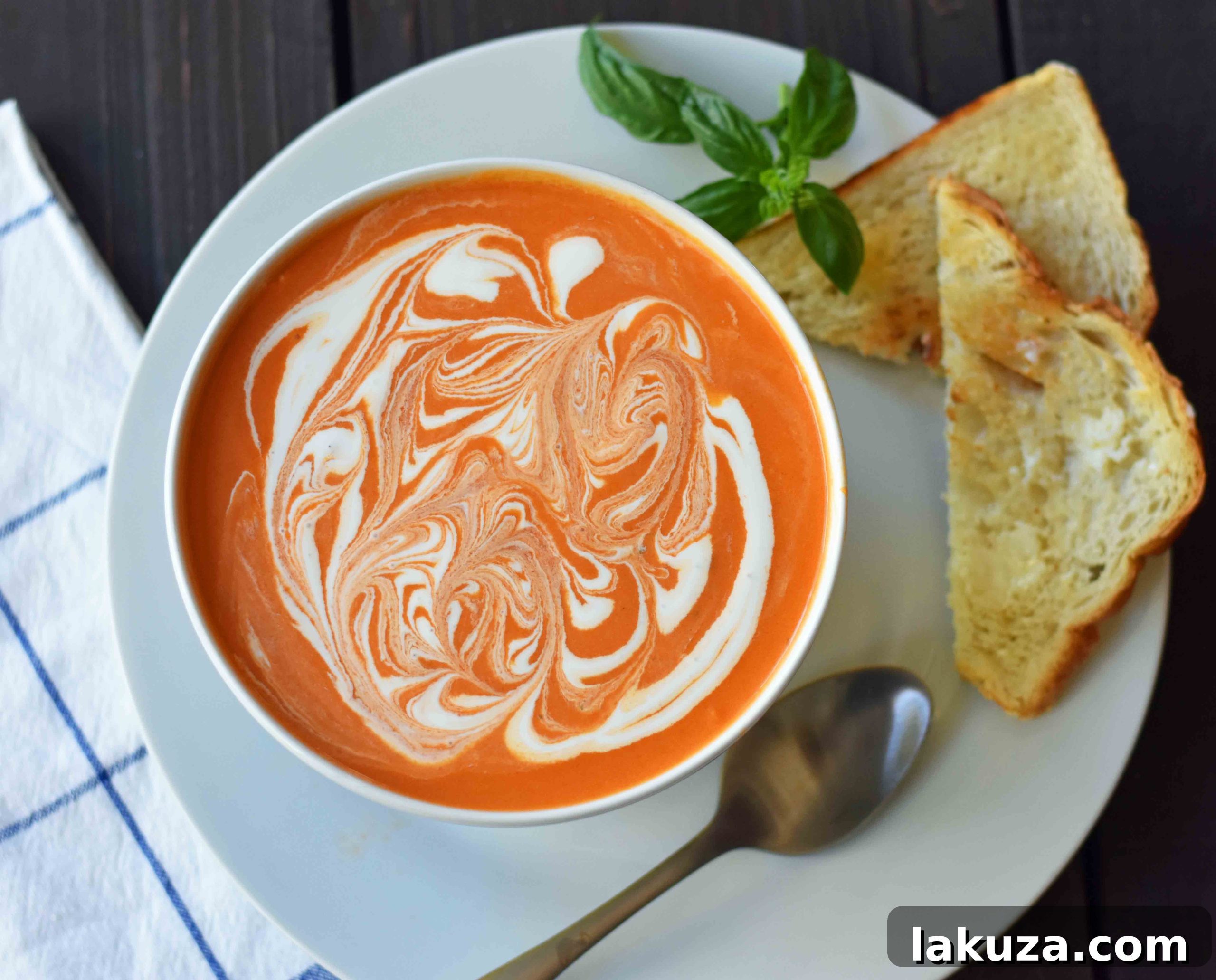 A bowl of the best homemade creamy tomato basil soup, garnished with fresh basil leaves and a swirl of cream. This comforting soup recipe is perfect for pairing with a crispy grilled cheese sandwich or crusty bread.