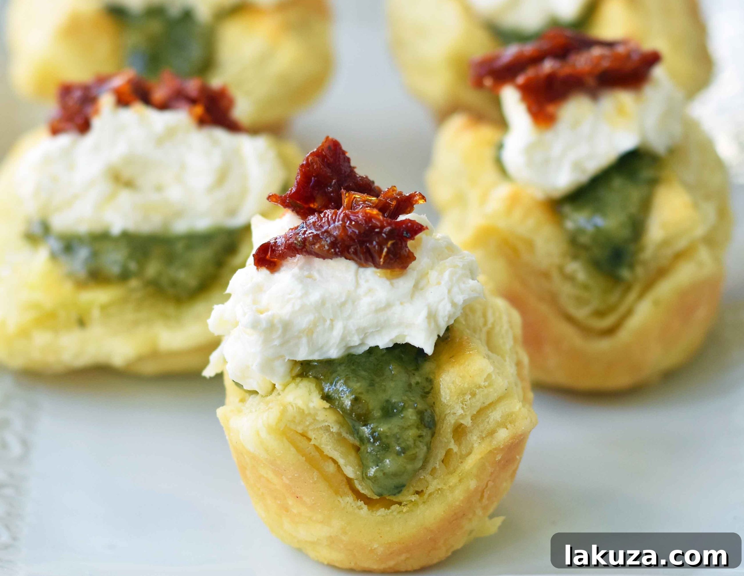 Close-up of Pesto Parmesan Sundried Tomato Tartlets, showcasing the layers of puff pastry, pesto, cheese, and tomatoes.