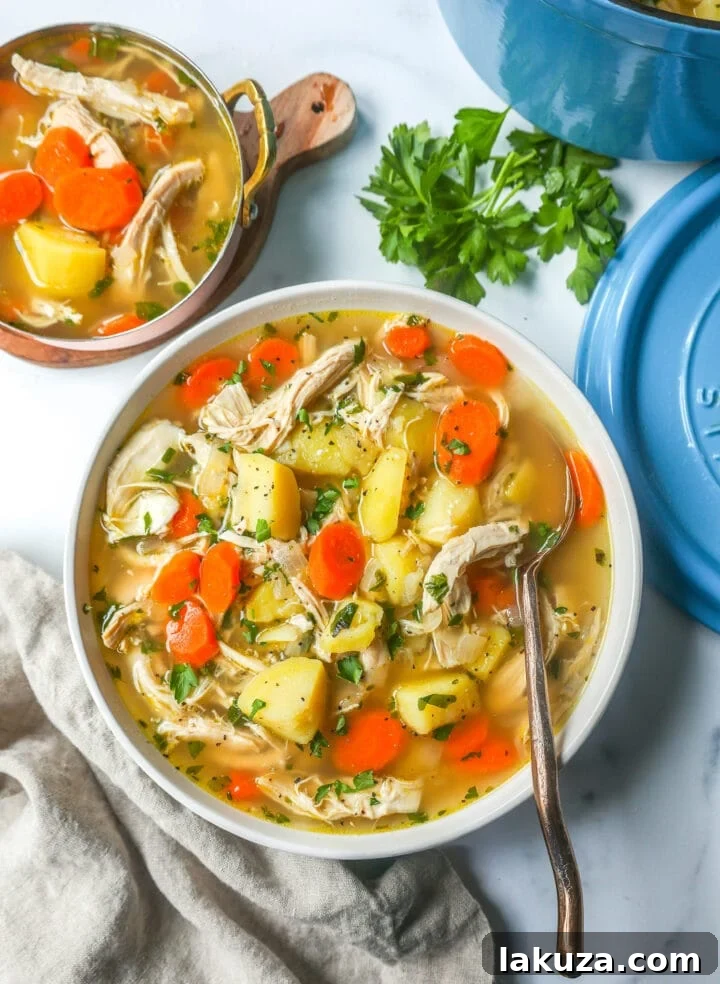 A steaming bowl of homemade chicken soup with carrots, potatoes, and parsley, ready to be enjoyed.