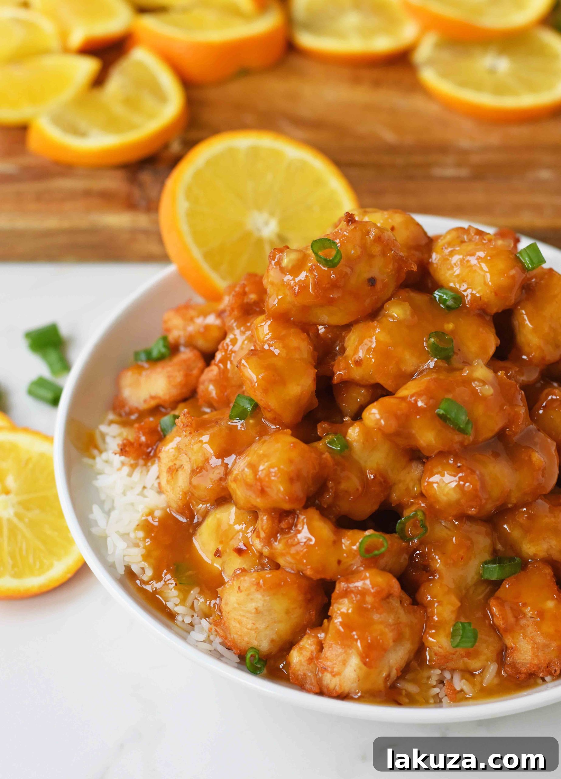 Plated homemade Chinese Orange Chicken with glossy orange sauce, garnished with green onions and orange zest.
