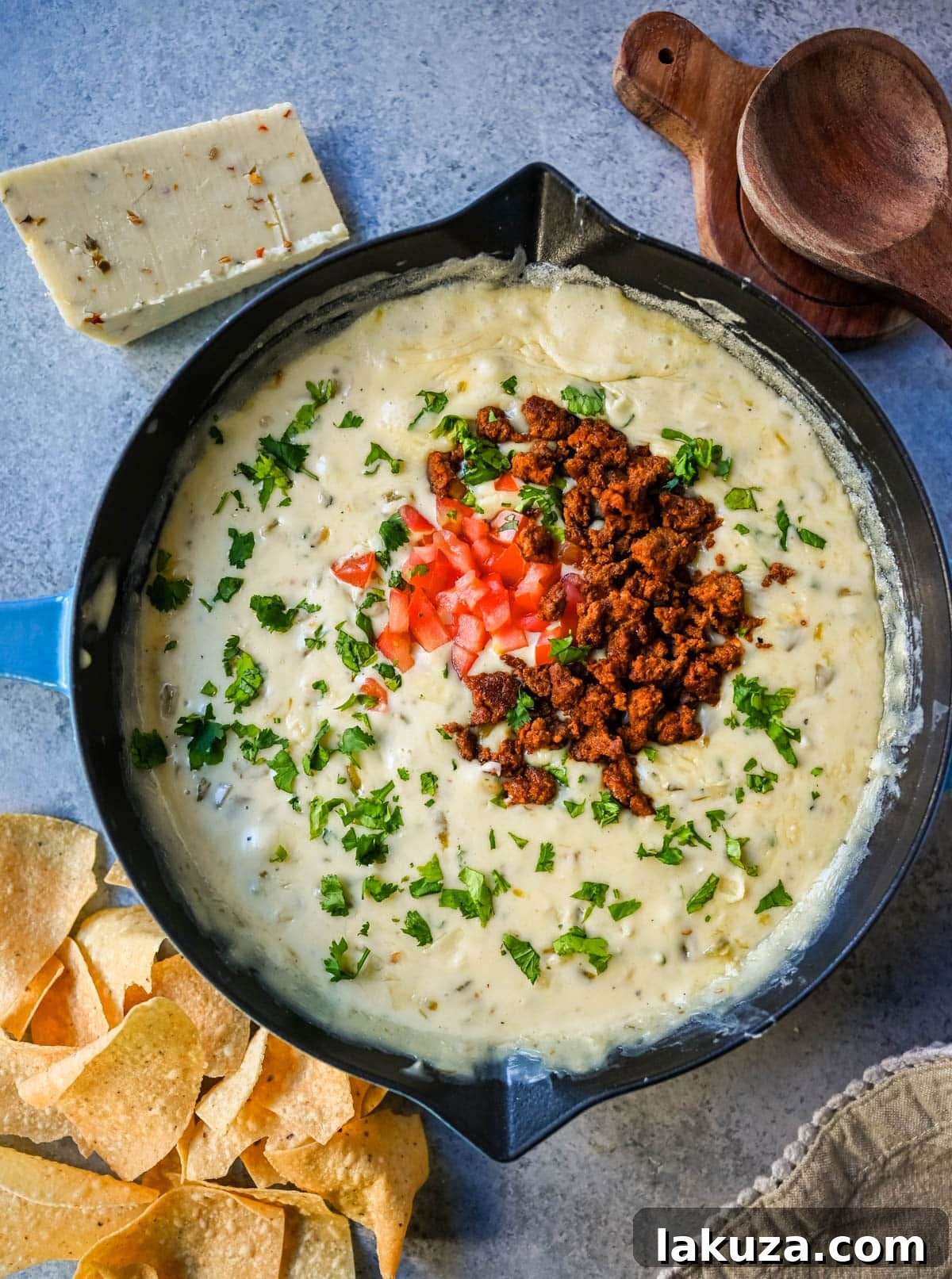 Ultimate Creamy Queso Dip 7 A vibrant platter featuring a bowl of white queso dip surrounded by an assortment of tortilla chips and fresh garnishes.