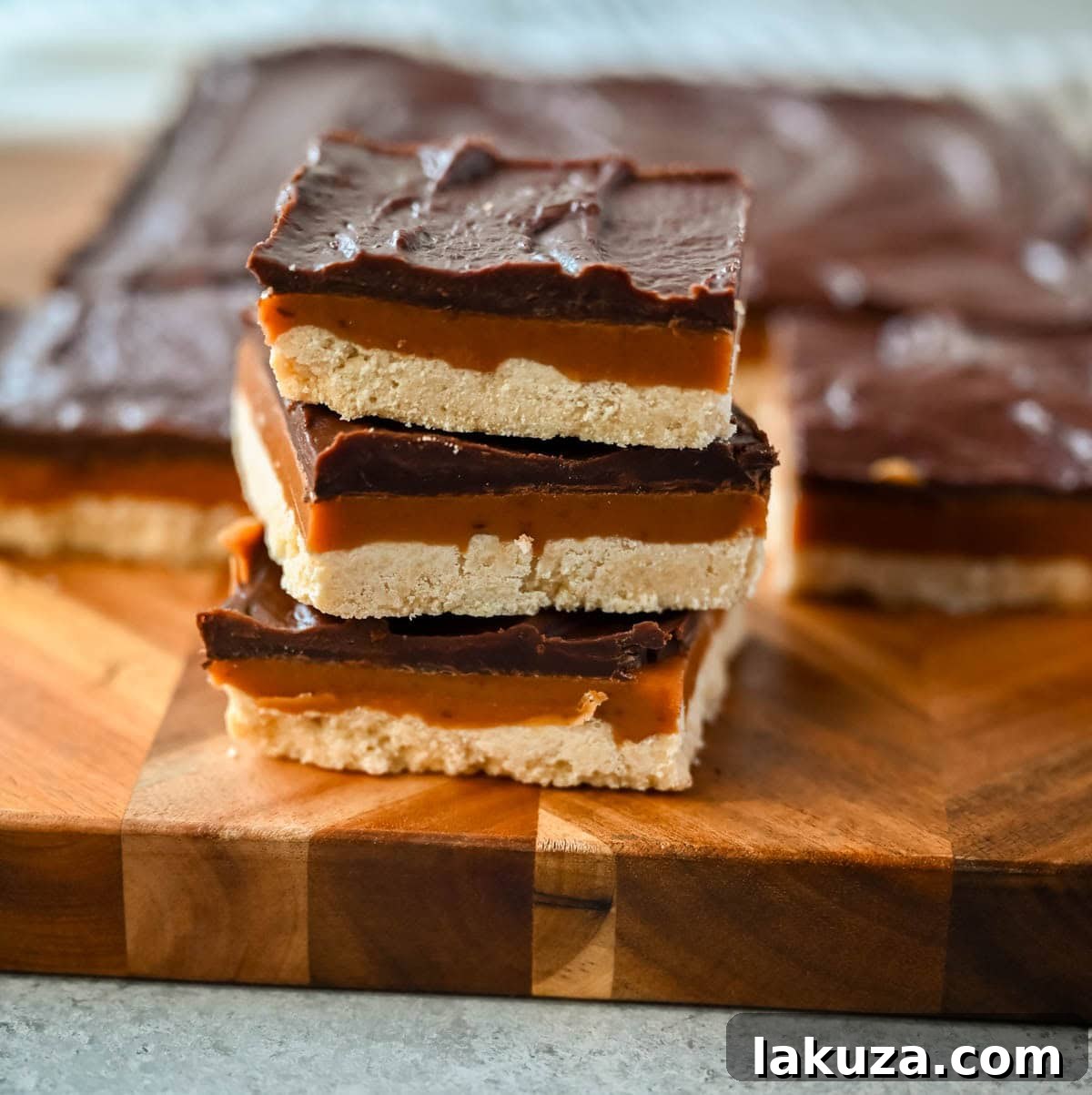 Decadent Millionaire Bars 5 A freshly cut Millionaire Bar, showcasing the clean layers of shortbread, caramel, and chocolate on a wooden cutting board.