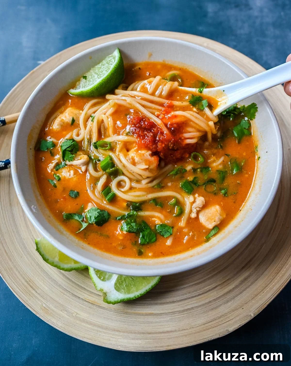 A close-up shot of a vibrant Chicken Curry Noodle Soup, featuring tender chicken pieces, bright yellow noodles, and fresh green cilantro in a creamy orange-hued broth. The bowl is garnished with lime wedges and more cilantro, highlighting its fresh ingredients.