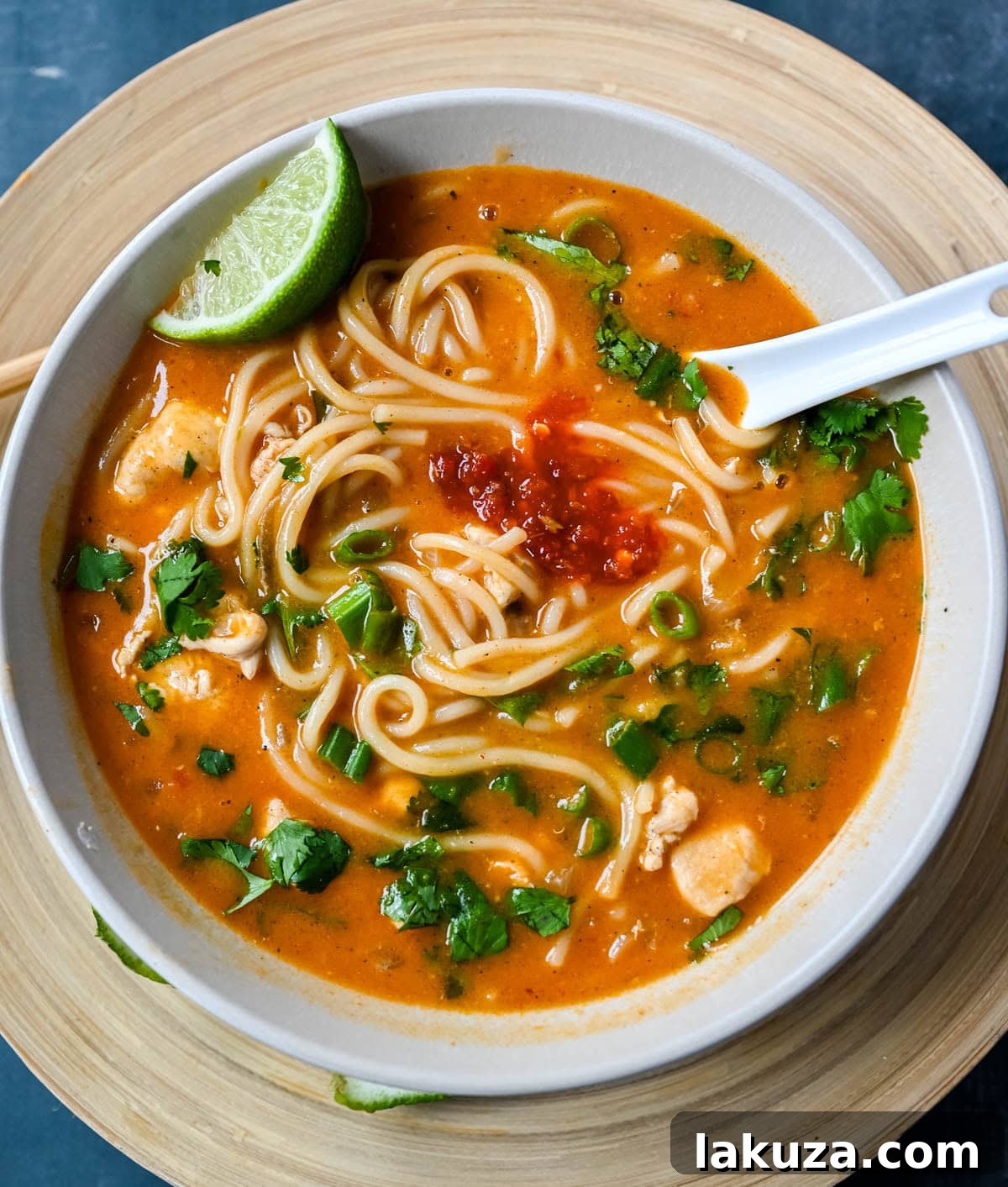 A bowl of vibrant Chicken Curry Noodle Soup garnished with fresh cilantro and a lime wedge, placed on a wooden table. The rich broth, tender chicken, and colorful noodles are clearly visible, inviting a taste.