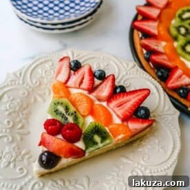 Fruit Pizza with a large, pizza-sized baked sugar cookie crust, topped with sweet cream cheese whipped cream and glazed fresh fruit.