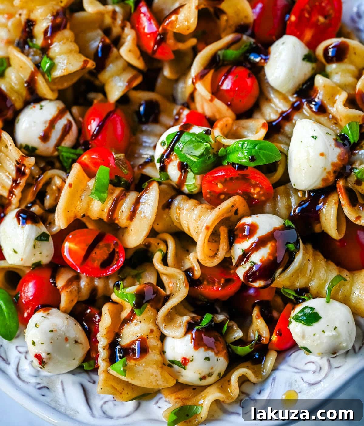 Close-up of Caprese pasta salad with a focus on halved grape tomatoes, basil, and mozzarella pearls.